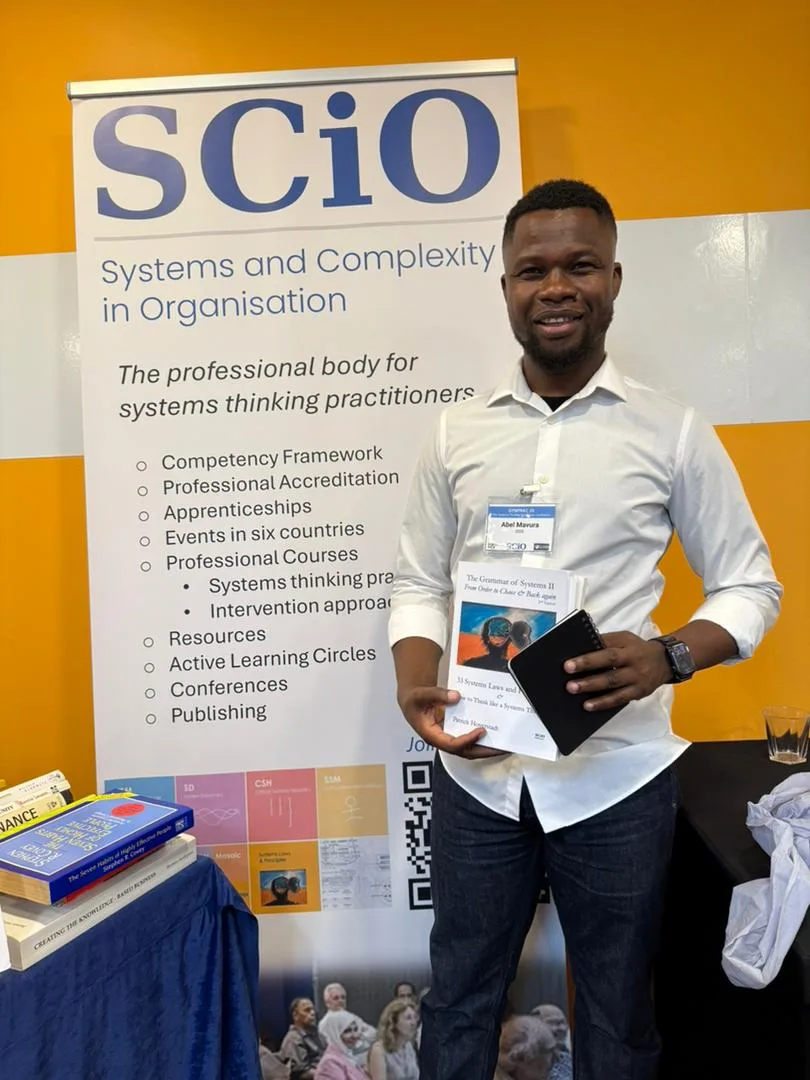 Abel Mavura holding publications at the SCiO — Systems and Complexity in Organisation — stand